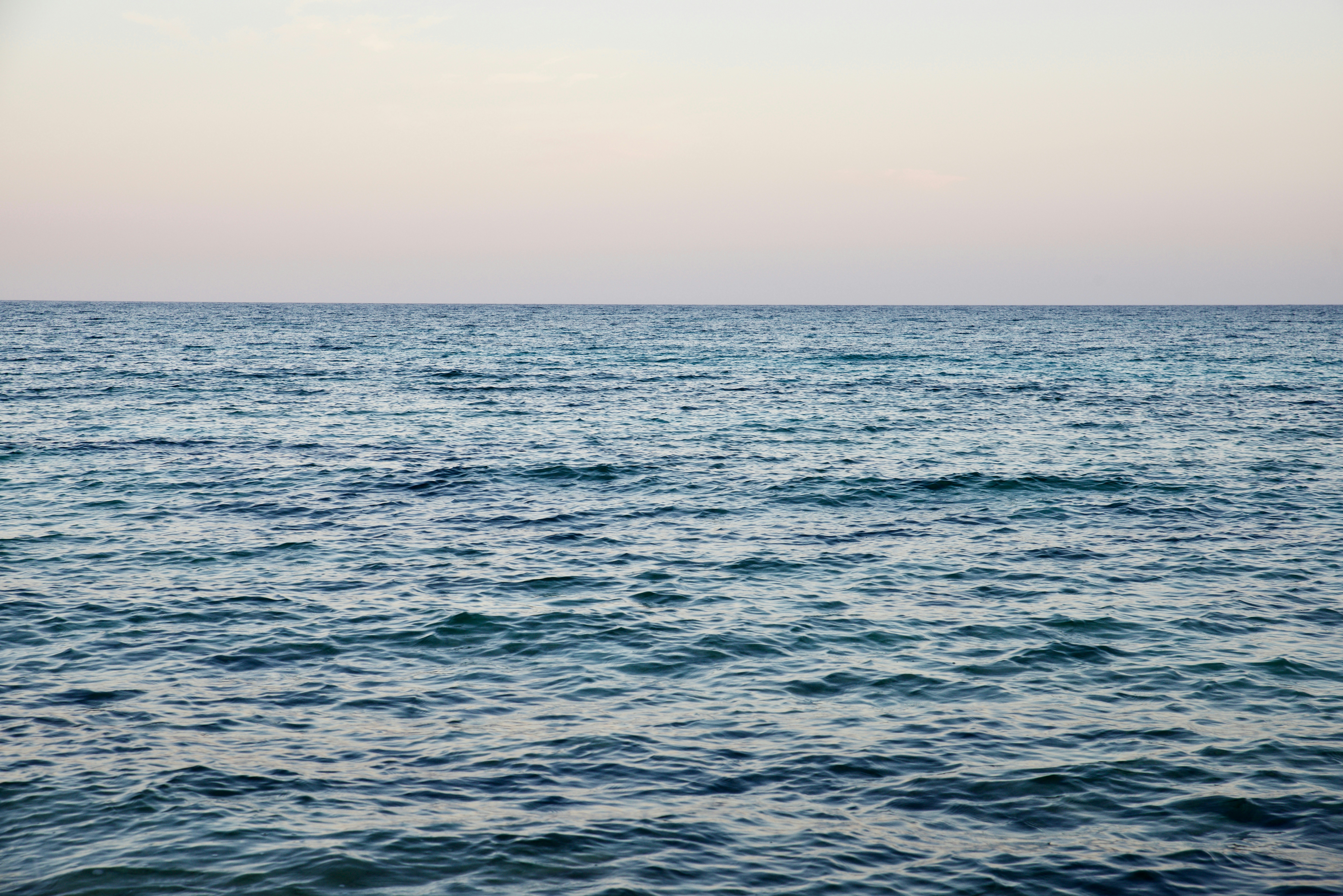 Calm ocean water stretches to the horizon under a pale sky, with gentle ripples reflecting soft light.